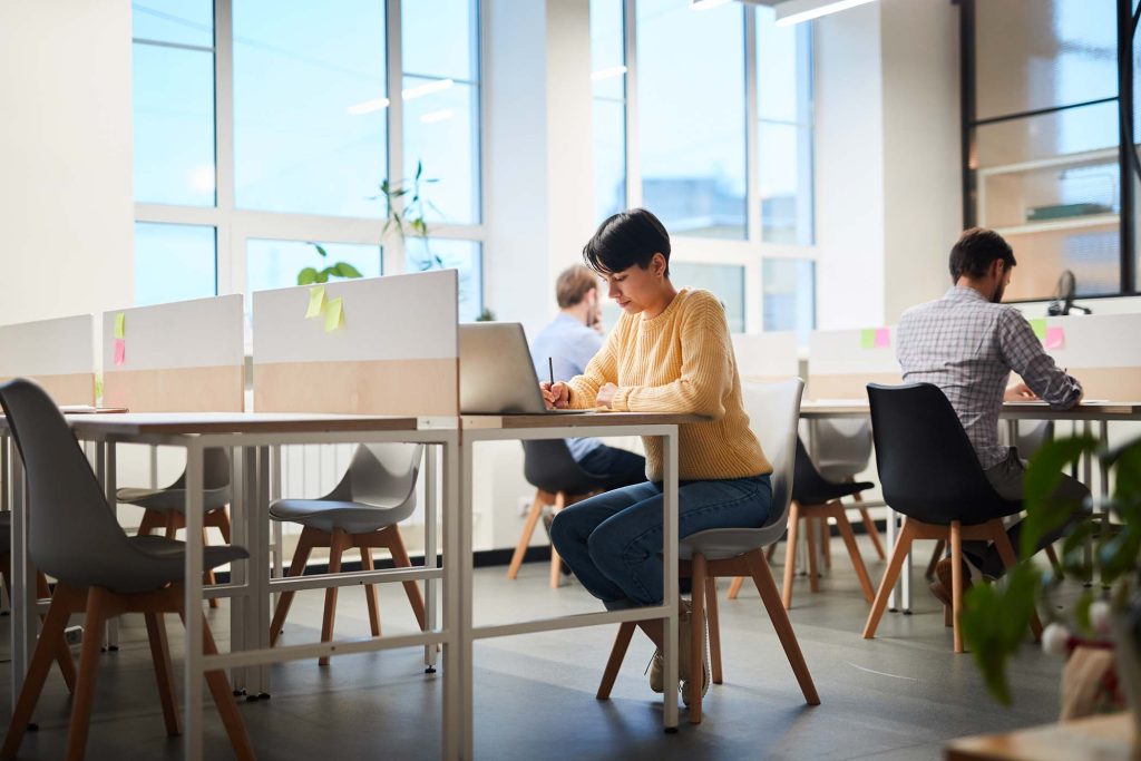 Serious busy student girl with short black hair sitting at table and using laptop while making important notes, she working on project in coworking space